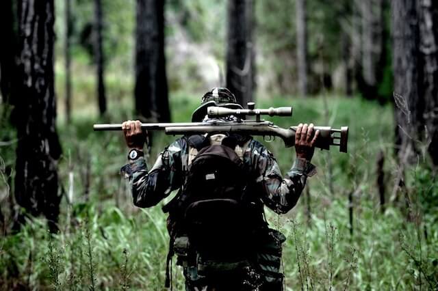 Bild av en Airsoft Sniper vandrandes genom terrängen med sitt gevär över axlarna.